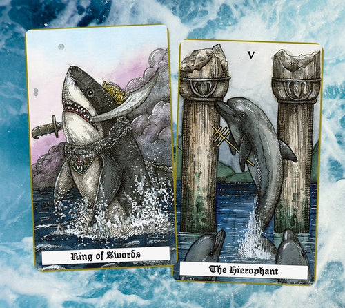 ocean deck tarot cards king of swords featuring a shark jumping out of water with sword in teeth and the hierophant card that features a dolphin jumping from wanter and standing between two pillars while two dolphins look up at it from the water.